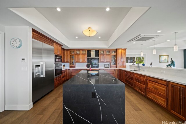 kitchen featuring brown cabinets, dark wood-type flooring, a sink, a tray ceiling, and appliances with stainless steel finishes