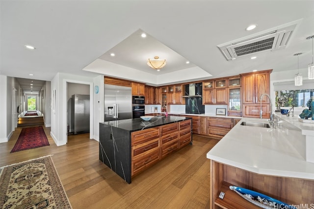 kitchen with stainless steel built in fridge, brown cabinets, a sink, black oven, and wall chimney exhaust hood