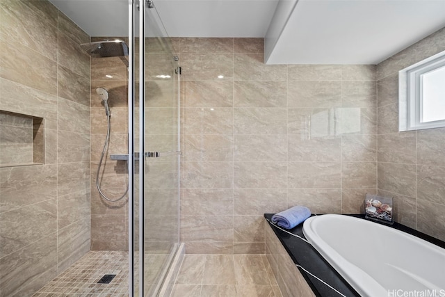 bathroom with tile walls, a bath, and a stall shower