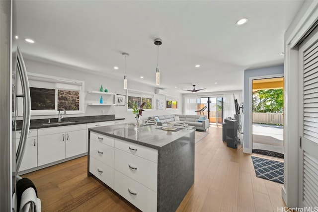 kitchen with a kitchen island with sink, white cabinets, wood-type flooring, and a sink