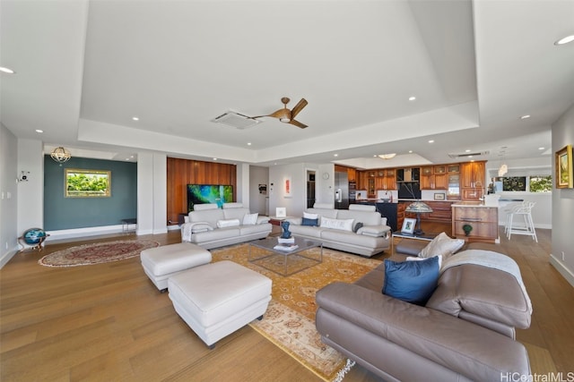 living area with a tray ceiling, recessed lighting, light wood-type flooring, and baseboards