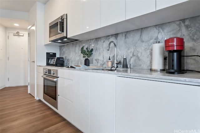 kitchen with light wood finished floors, white cabinets, appliances with stainless steel finishes, a sink, and backsplash