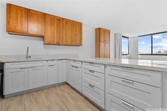 kitchen featuring light stone counters, a sink, white cabinetry, light wood-type flooring, and brown cabinetry