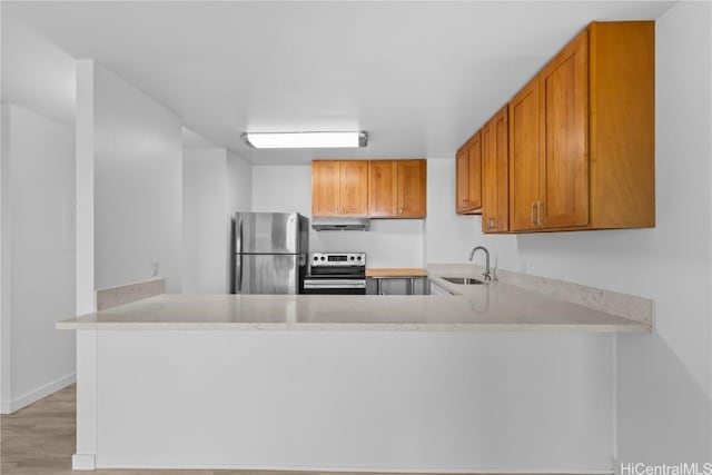 kitchen featuring stainless steel appliances, brown cabinetry, a sink, a peninsula, and under cabinet range hood