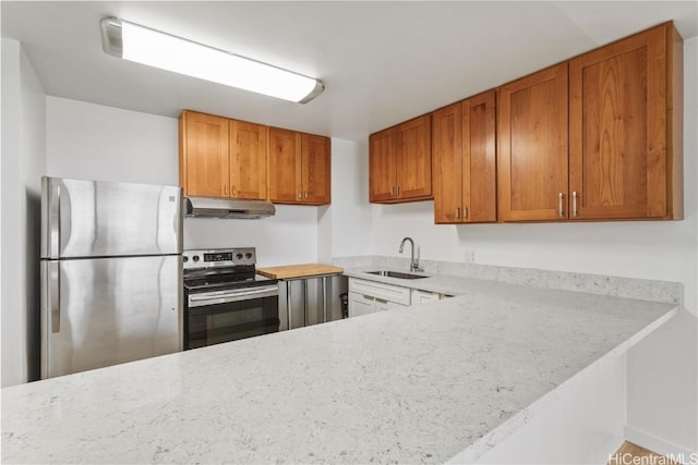 kitchen featuring under cabinet range hood, a peninsula, a sink, light countertops, and appliances with stainless steel finishes