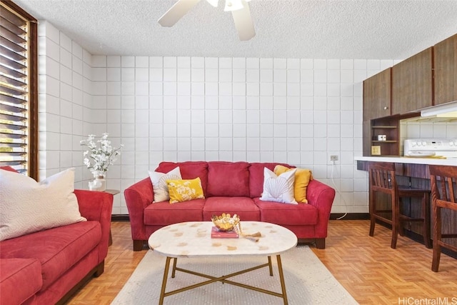 living room with ceiling fan, a textured ceiling, and tile walls