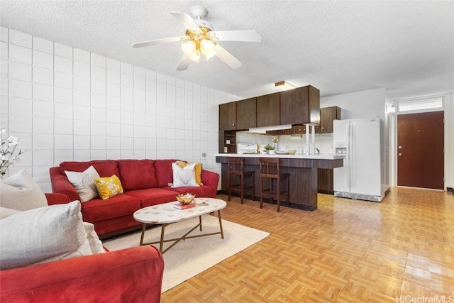 living area with tile walls, ceiling fan, and a textured ceiling