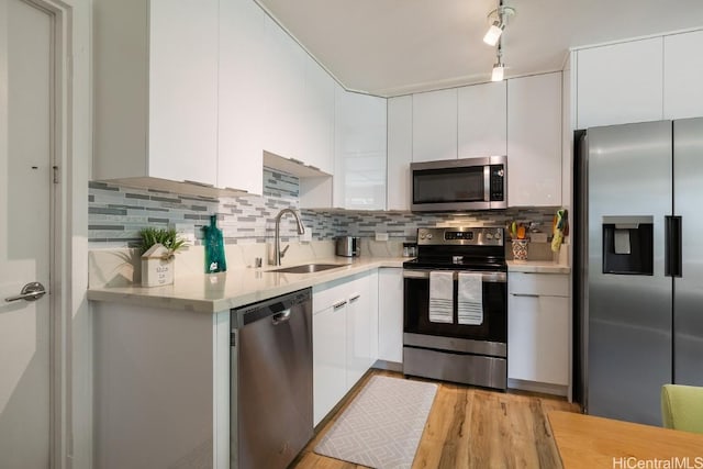 kitchen with stainless steel appliances, a sink, white cabinets, light countertops, and backsplash