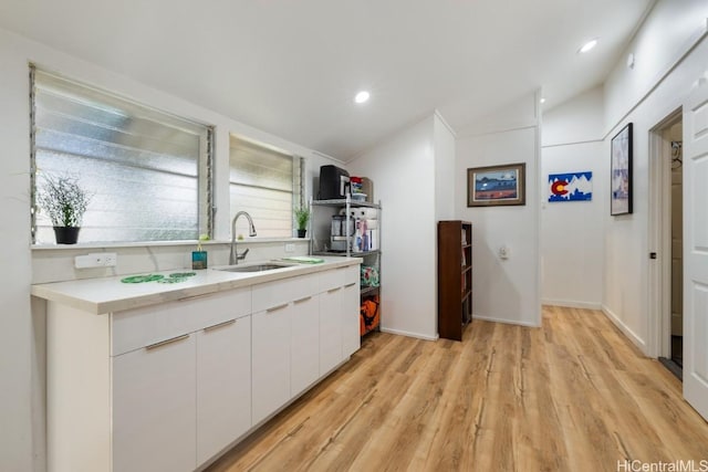 kitchen with a sink, white cabinets, vaulted ceiling, light countertops, and light wood-type flooring