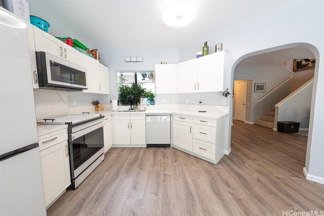 kitchen with arched walkways, white appliances, a sink, white cabinetry, and light countertops