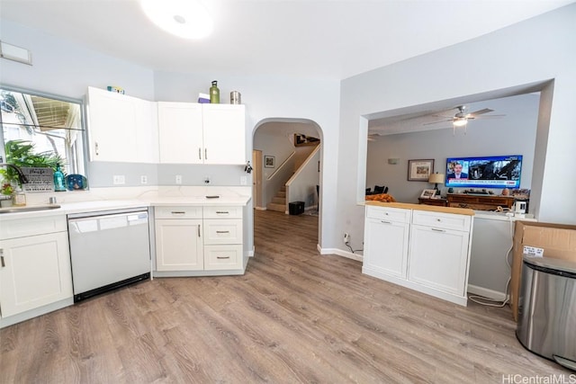 kitchen featuring arched walkways, a sink, white cabinets, light countertops, and dishwasher