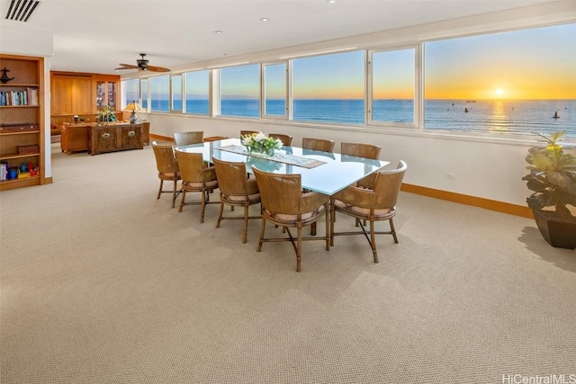 dining space featuring a water view, light colored carpet, and a beach view