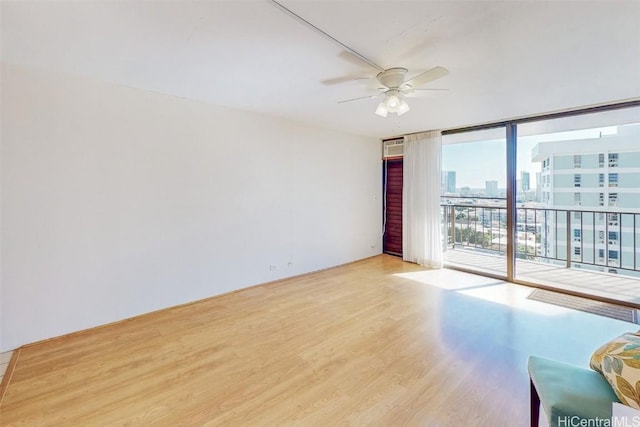 unfurnished room featuring a view of city, ceiling fan, a wall of windows, and wood finished floors