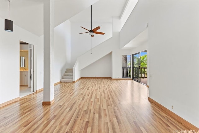 unfurnished living room with ceiling fan, light wood-type flooring, and a high ceiling