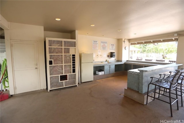 kitchen with concrete flooring, recessed lighting, a peninsula, freestanding refrigerator, and a kitchen bar