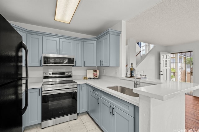 kitchen featuring light countertops, appliances with stainless steel finishes, a sink, a textured ceiling, and a peninsula