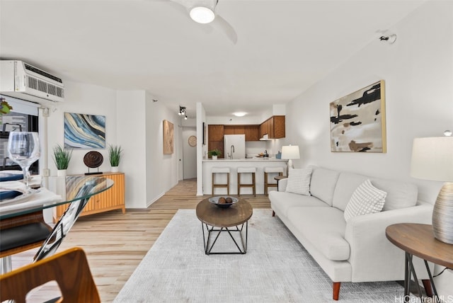 living room with a wall mounted air conditioner, ceiling fan, and light hardwood / wood-style flooring