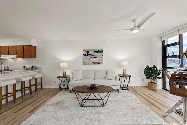 living room with ceiling fan, light hardwood / wood-style flooring, sink, and floor to ceiling windows