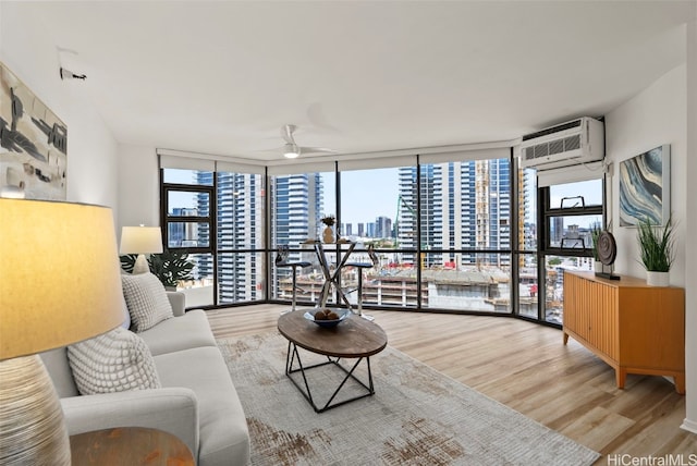 living room featuring a wall unit AC, a wall of windows, light wood-type flooring, and ceiling fan