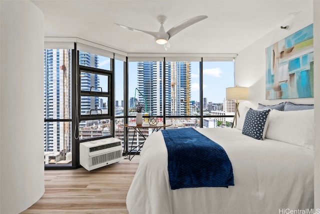 bedroom with an AC wall unit, a wall of windows, and hardwood / wood-style floors