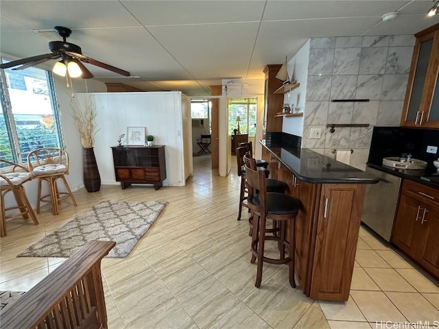 kitchen featuring tasteful backsplash, a kitchen breakfast bar, dishwasher, ceiling fan, and light tile patterned floors