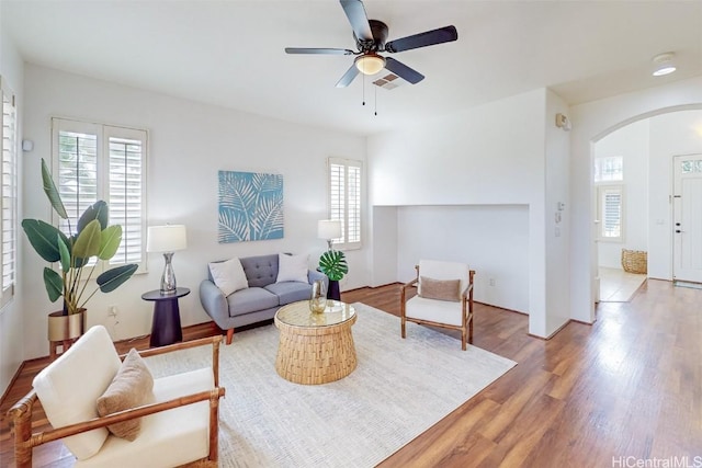 living room featuring a ceiling fan, plenty of natural light, arched walkways, and wood finished floors