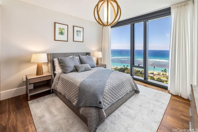 bedroom featuring a water view, wood finished floors, a view of the beach, and baseboards