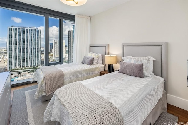 bedroom with a view of city, floor to ceiling windows, baseboards, and wood finished floors