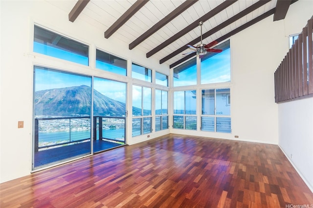 empty room with beamed ceiling, a mountain view, wood finished floors, a ceiling fan, and high vaulted ceiling
