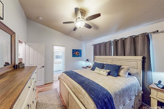 bedroom with vaulted ceiling, ceiling fan, light wood finished floors, and ensuite bath