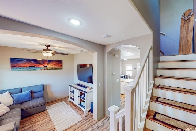 living room with light wood-style floors, arched walkways, ceiling fan, and stairway