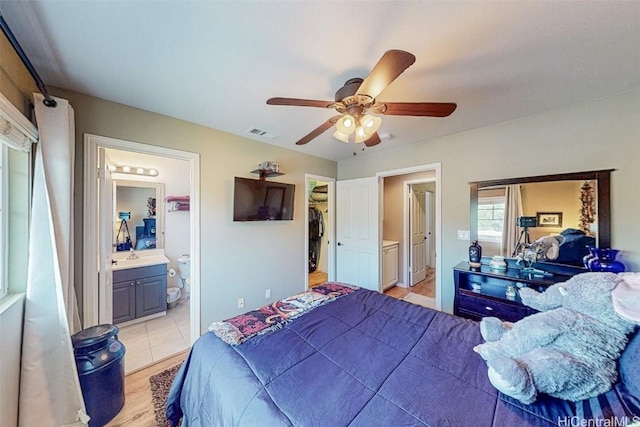 bedroom with ceiling fan, connected bathroom, visible vents, light wood-type flooring, and a walk in closet