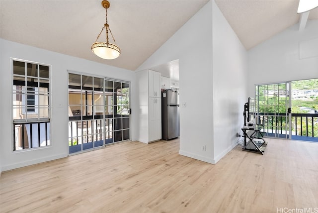 spare room with high vaulted ceiling, plenty of natural light, light wood-style flooring, and baseboards