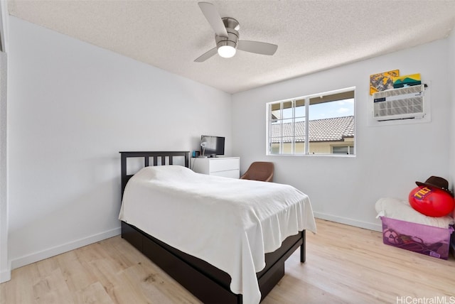 bedroom with a ceiling fan, an AC wall unit, a textured ceiling, wood finished floors, and baseboards