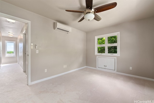 spare room featuring a ceiling fan, a wall unit AC, light carpet, and baseboards