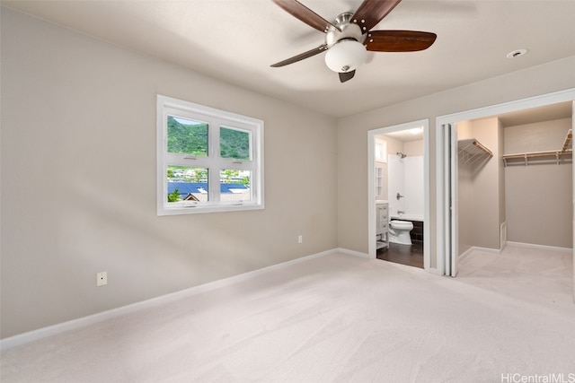 unfurnished bedroom featuring light carpet, baseboards, ensuite bathroom, a spacious closet, and a closet