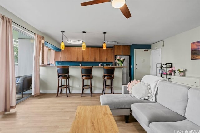 living area featuring ceiling fan, baseboards, and light wood-style floors