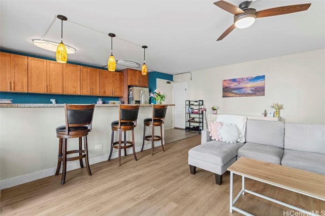 living room featuring ceiling fan, light wood-type flooring, and baseboards