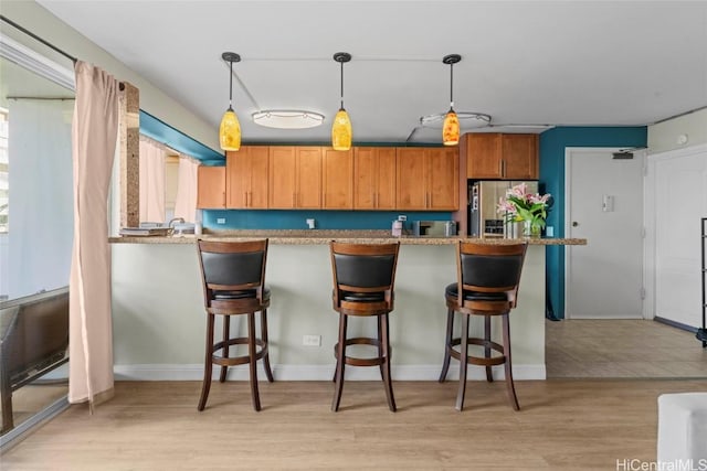 kitchen featuring light wood-style floors, a breakfast bar area, decorative light fixtures, and stainless steel fridge with ice dispenser