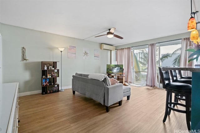 living room with an AC wall unit, ceiling fan, light wood-style flooring, and baseboards