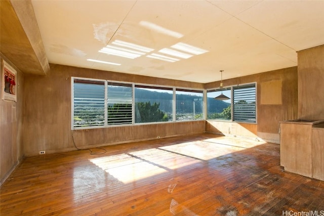 unfurnished room featuring wooden walls, a mountain view, and wood finished floors