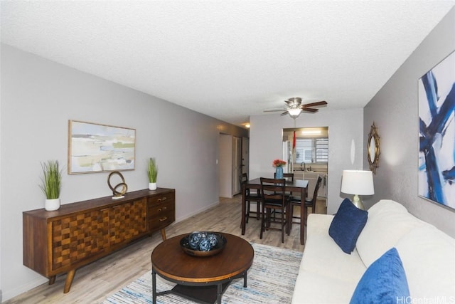 living area featuring light wood-type flooring, ceiling fan, and a textured ceiling