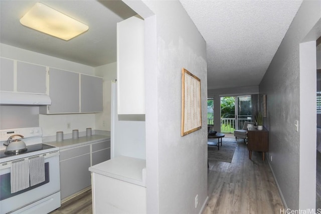 kitchen with a textured ceiling, under cabinet range hood, electric range, wood finished floors, and light countertops