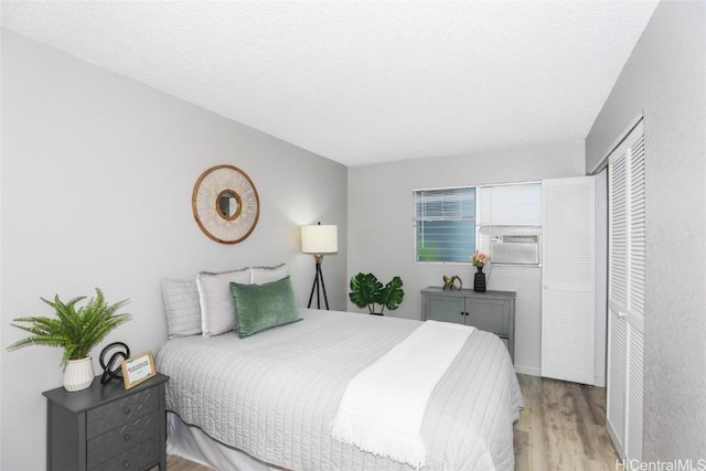 bedroom with cooling unit, a closet, light wood-style flooring, and a textured ceiling