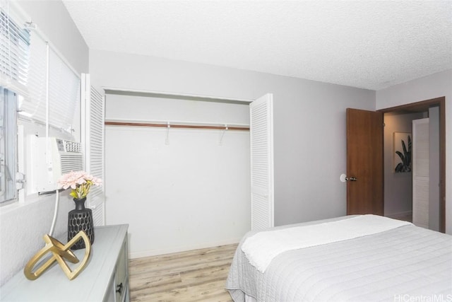 bedroom featuring light wood-type flooring, a textured ceiling, cooling unit, and a closet