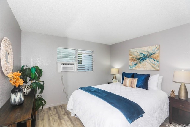 bedroom featuring a textured ceiling, cooling unit, wood finished floors, and baseboards