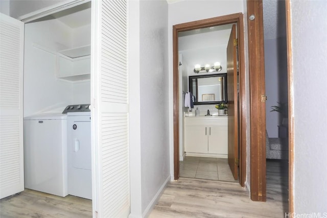 clothes washing area featuring laundry area, a sink, independent washer and dryer, and light wood finished floors