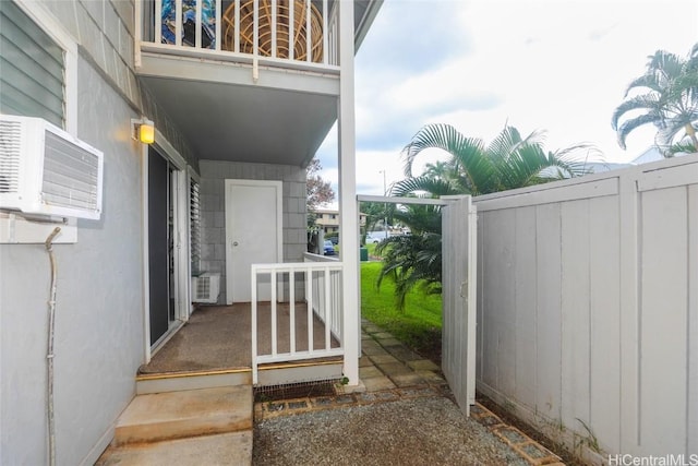 entrance to property featuring an AC wall unit, fence, and a balcony