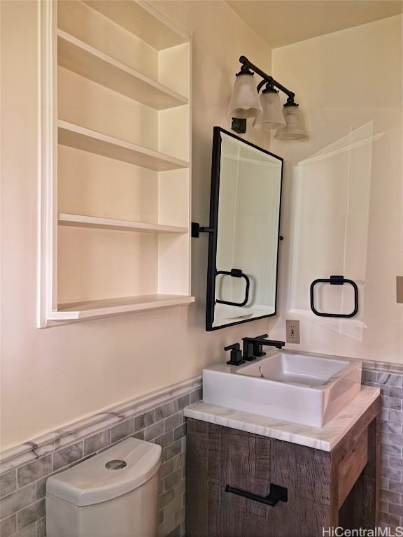 half bath with wainscoting, tile walls, vanity, and toilet