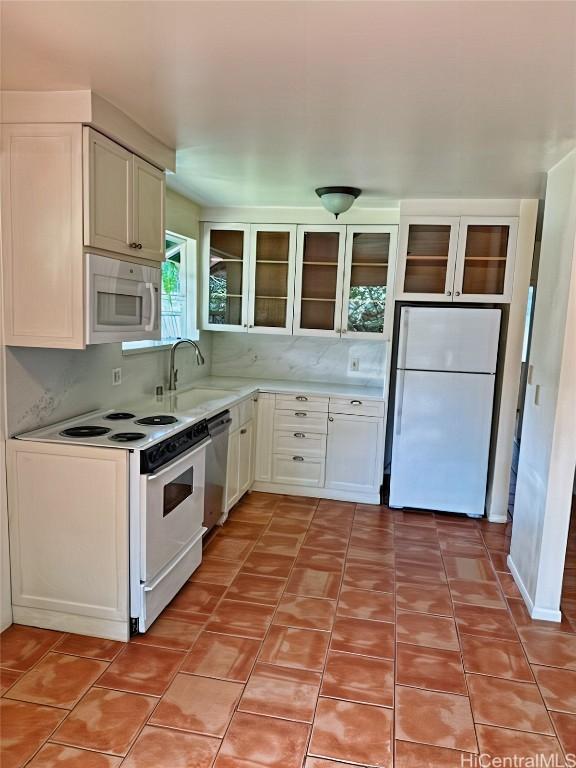 kitchen with backsplash, glass insert cabinets, light countertops, white appliances, and a sink